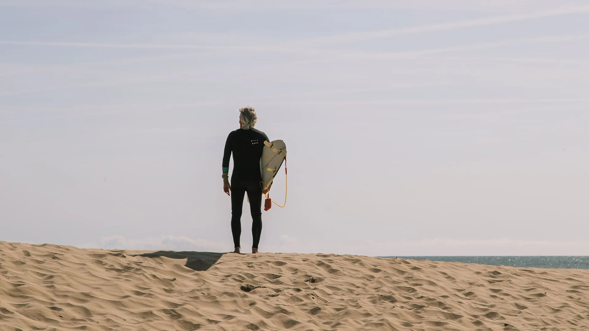 265 días sin olas: un surfista con su tabla mira al mar desde lo alto de una duna