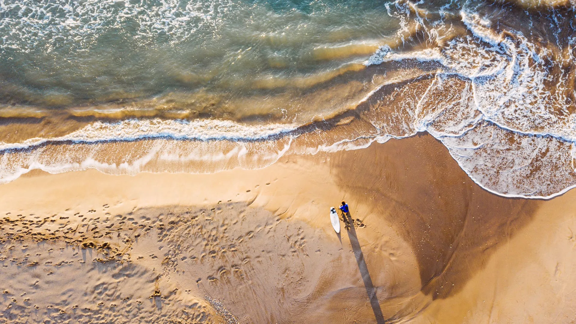 265 días sin olas: vista aérea de un surfista con su tabla en la orilla
