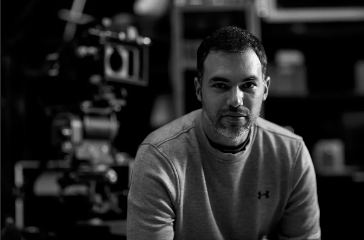 Retrato en blanco y negro del director Adrian Egea, con una cámara de cine detrás