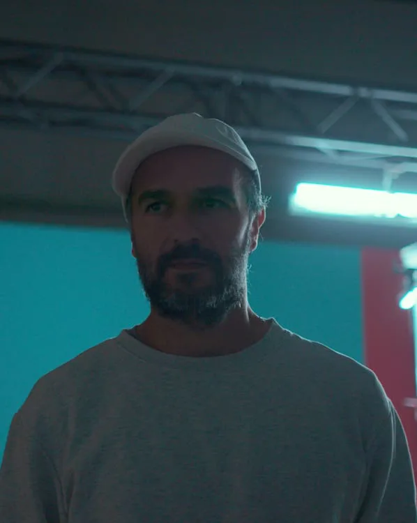 Hombre con gorra blanca en un plató iluminado en turquesa y rojo, del trabajo de Alberto Arellano