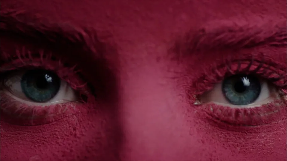 Fotograma de un trabajo de Alberto Arellano: primer plano de unos ojos claros en un rostro cubierto de polvo magenta