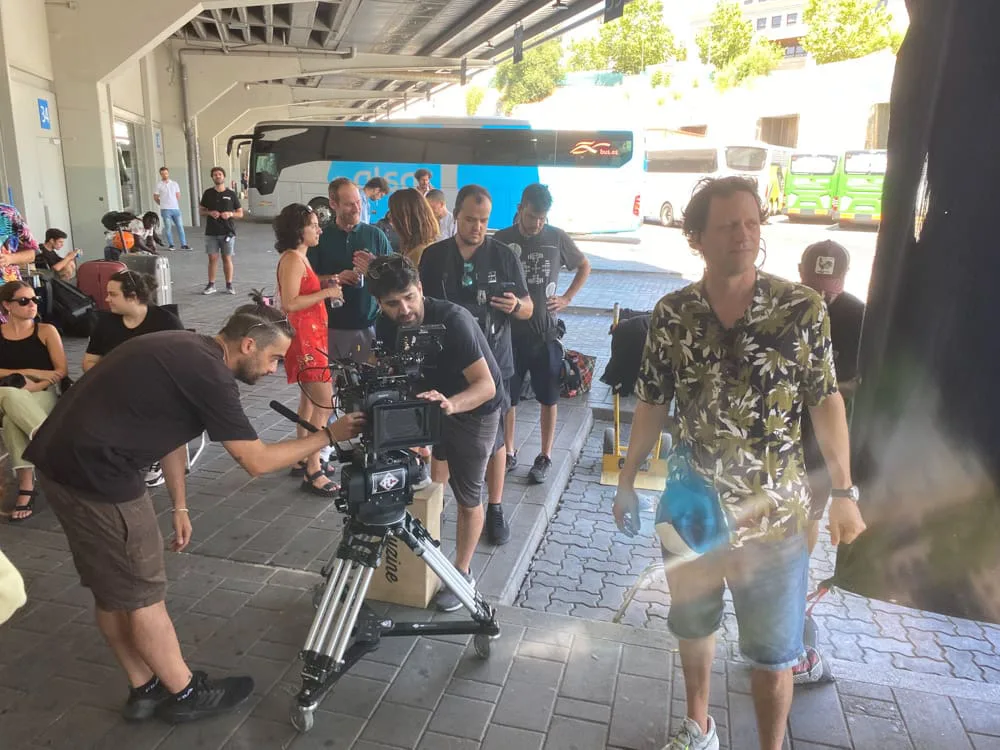 Alsa, making of: cámara en trípode en una estación de autobuses, con equipo y reparto alrededor