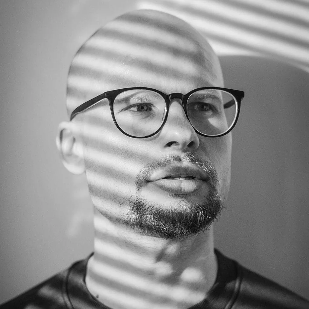 Retrato en blanco y negro de un hombre con gafas y sombras de persiana, Arminas Valunas