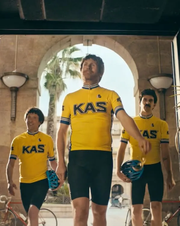 Ciclistas con maillot amarillo de KAS caminan bajo un arco, en un anuncio de Bernat Lliteras