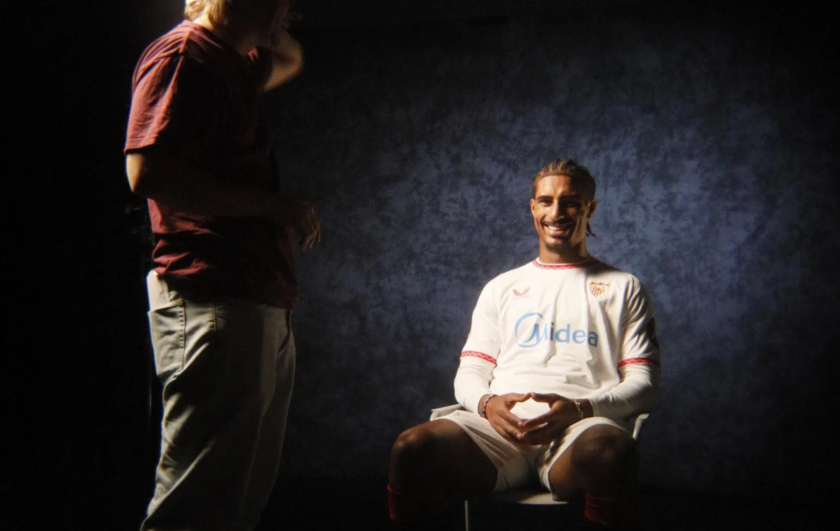 Congelados x Sevilla FC: smiling Sevilla FC player seated under a spotlight beside a crew member