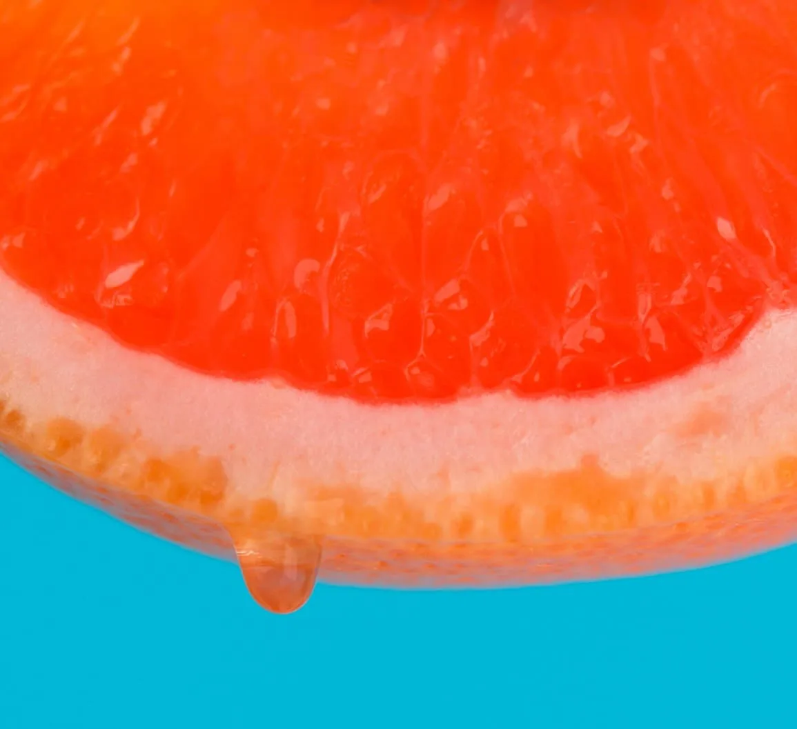 Rodaja de pomelo goteando sobre fondo azul, de un anuncio de bodegón de Esther Padial