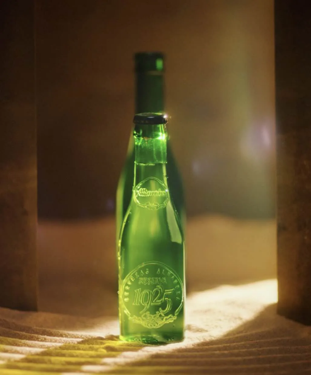 Botella de Alhambra Reserva 1925 sobre arena con luz cálida, de un anuncio de Esther Padial
