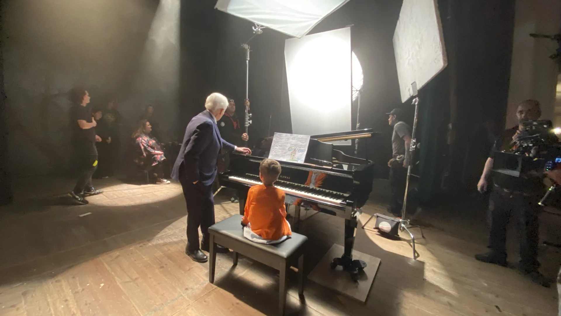 Rodaje de Imparables para la Fundación Josep Carreras: un hombre mayor con traje junto a un niño al piano