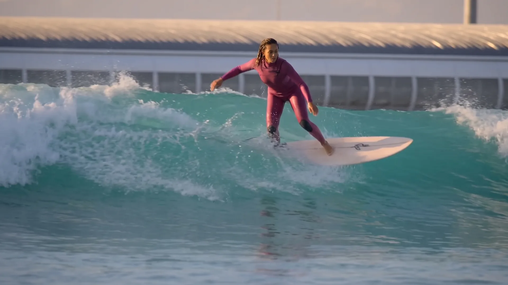Gemswell Society, película con IA: una surfista con neopreno rosa coge una ola en la laguna