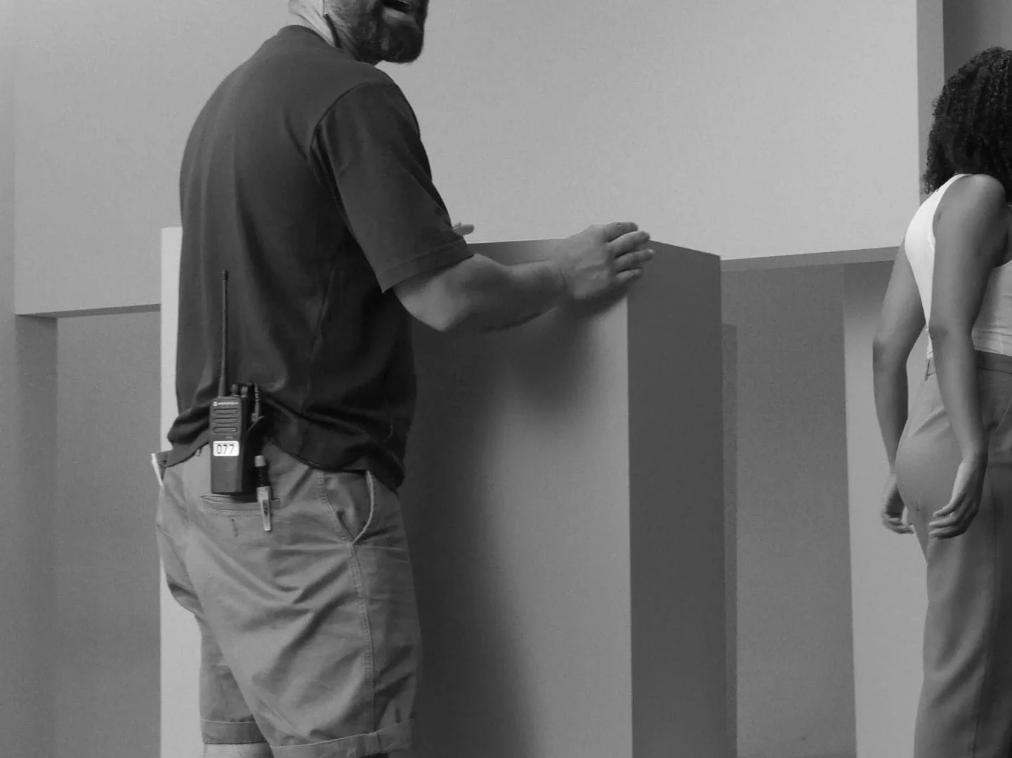 Making of de ISDIN Acniben: técnico con walkie moviendo bloques de decorado, en blanco y negro