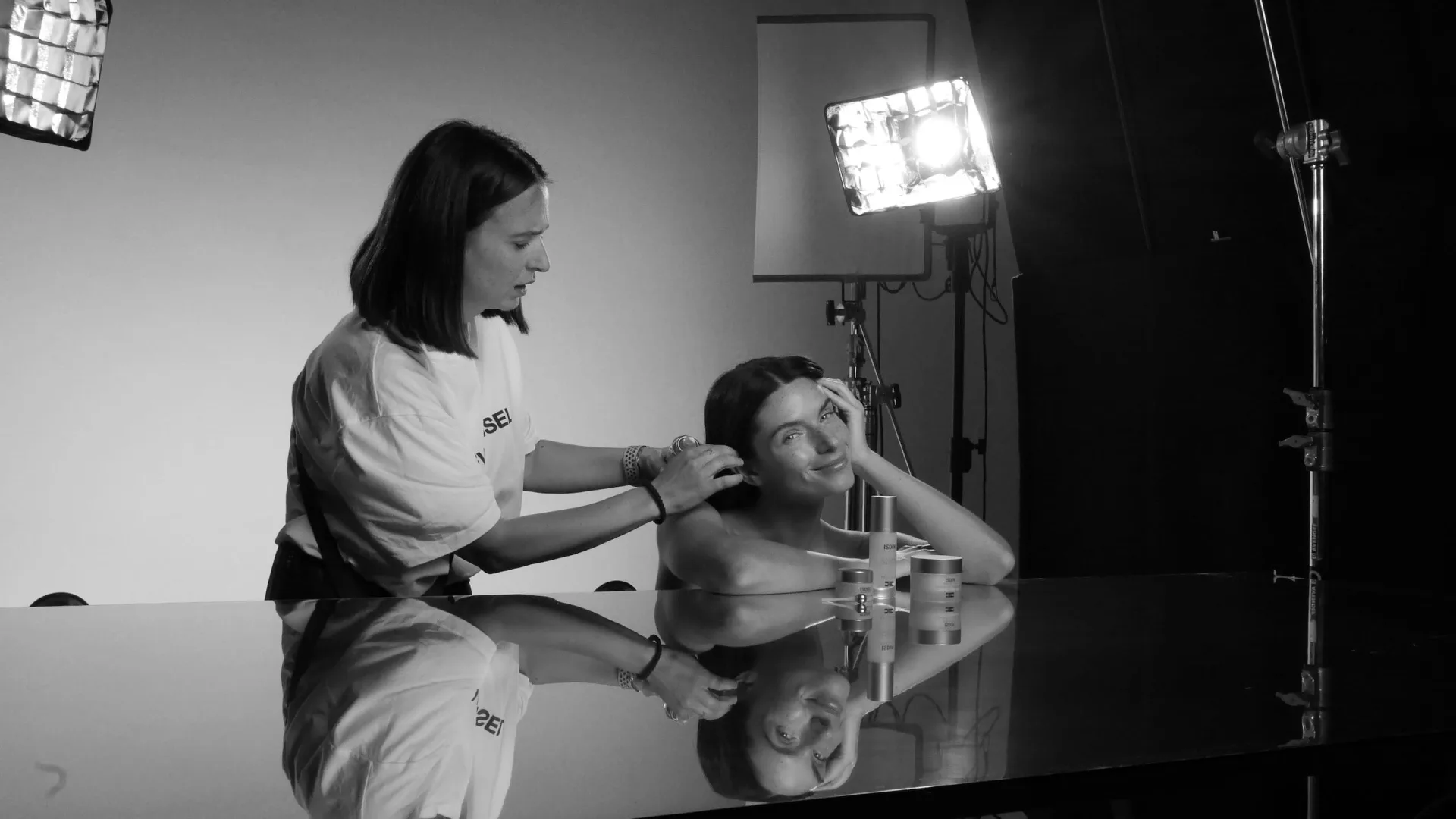 Isdin Hyaluronic shoot: hairstylist adjusting the model's hair beside a mirrored table, black and white