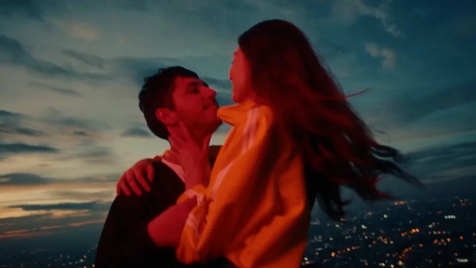 Fotograma de un trabajo de Juan Pablo Caballero: una pareja se abraza al anochecer sobre las luces de la ciudad