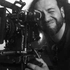 El director Marco de Aguilar mirando por el visor de una cámara de cine, en blanco y negro