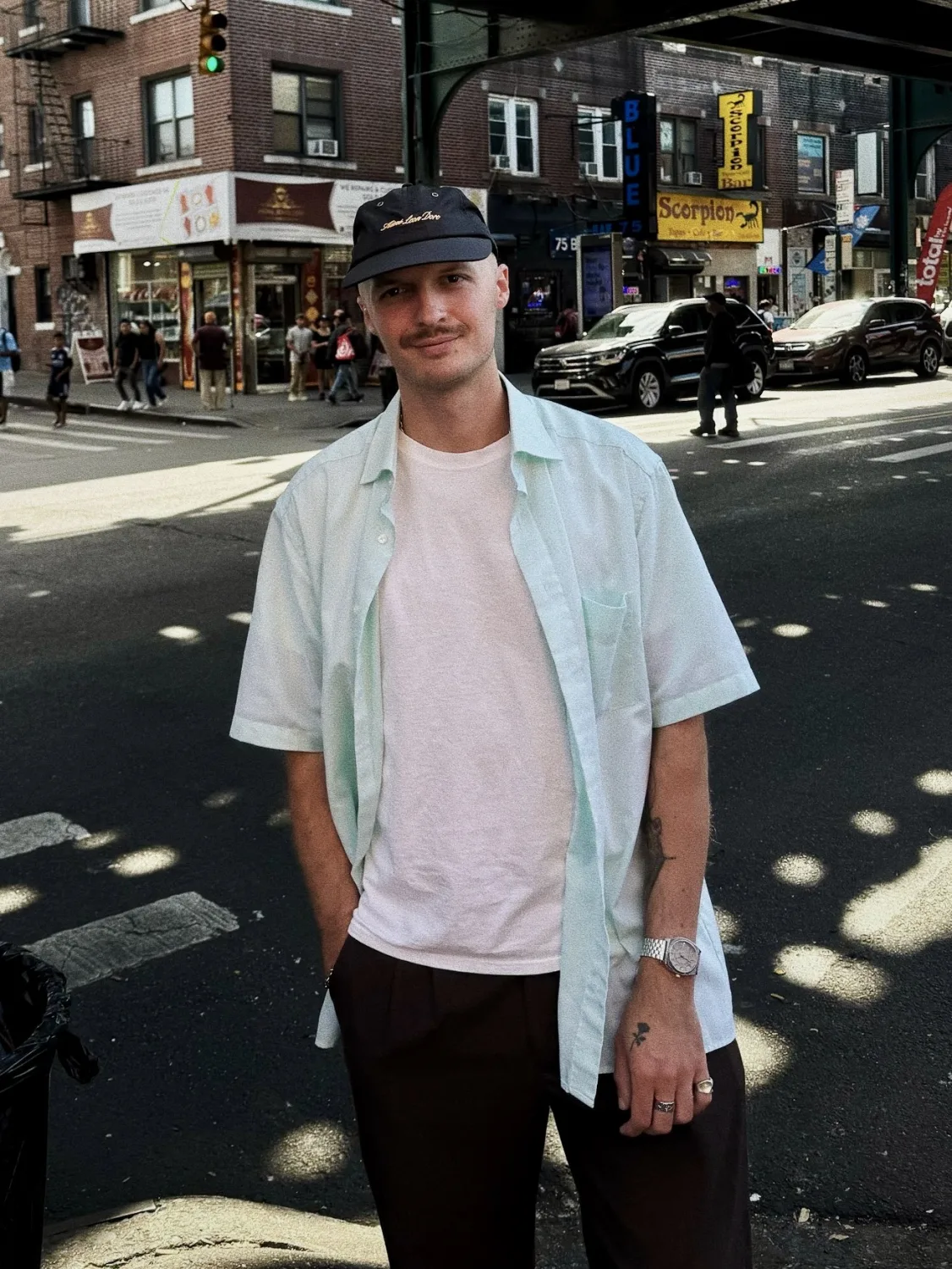 Retrato de Miljak en la calle, con gorra y camisa abierta, en una esquina soleada