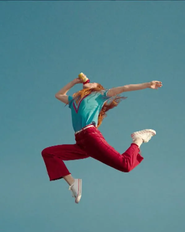 Frame from a commercial by Pedro Abreu: a woman leaps against a blue sky while drinking