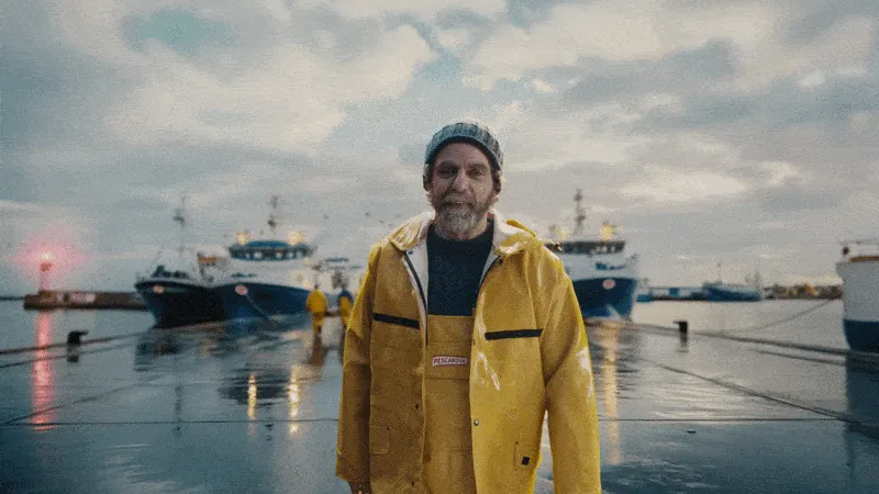 Pescanova commercial still: fisherman in yellow oilskins walking along a rainy dock at dusk