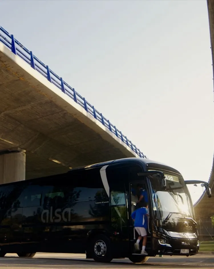 Autocar de Alsa bajo un puente mientras sube un jugador, de un anuncio de Sonia Ramirez