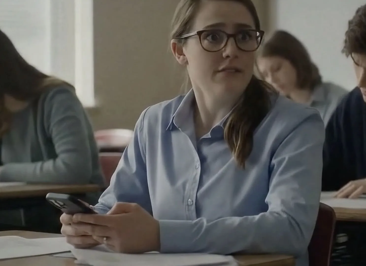The death of visual evidence, AI-generated frame: worried student holding a phone at her classroom desk