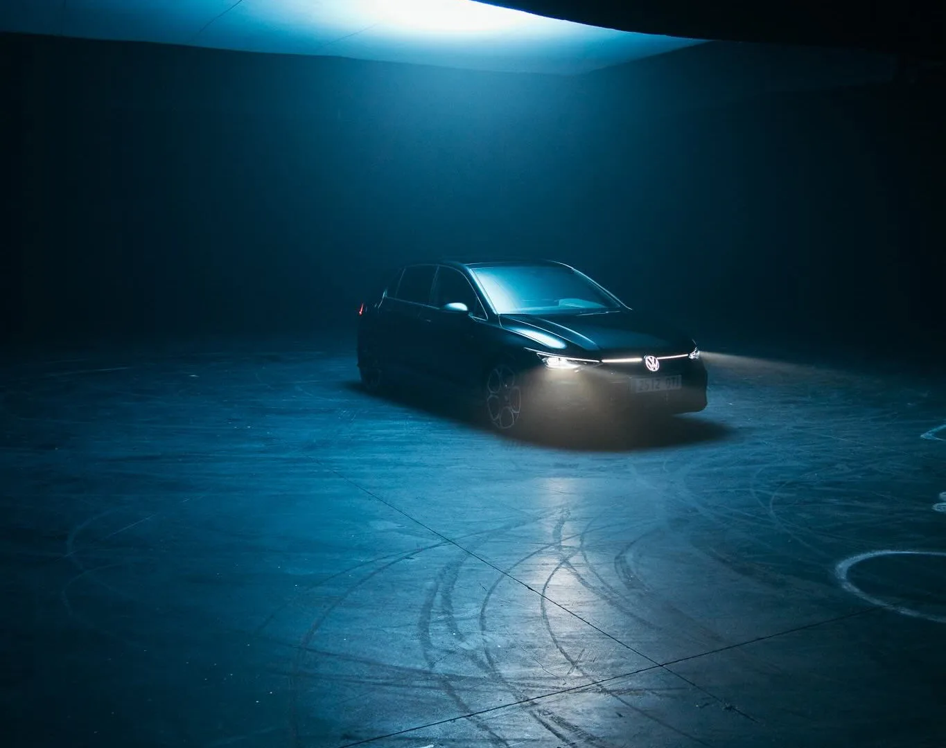 Volkswagen Golf GTI with headlights on in a hazy studio, drift marks on the floor