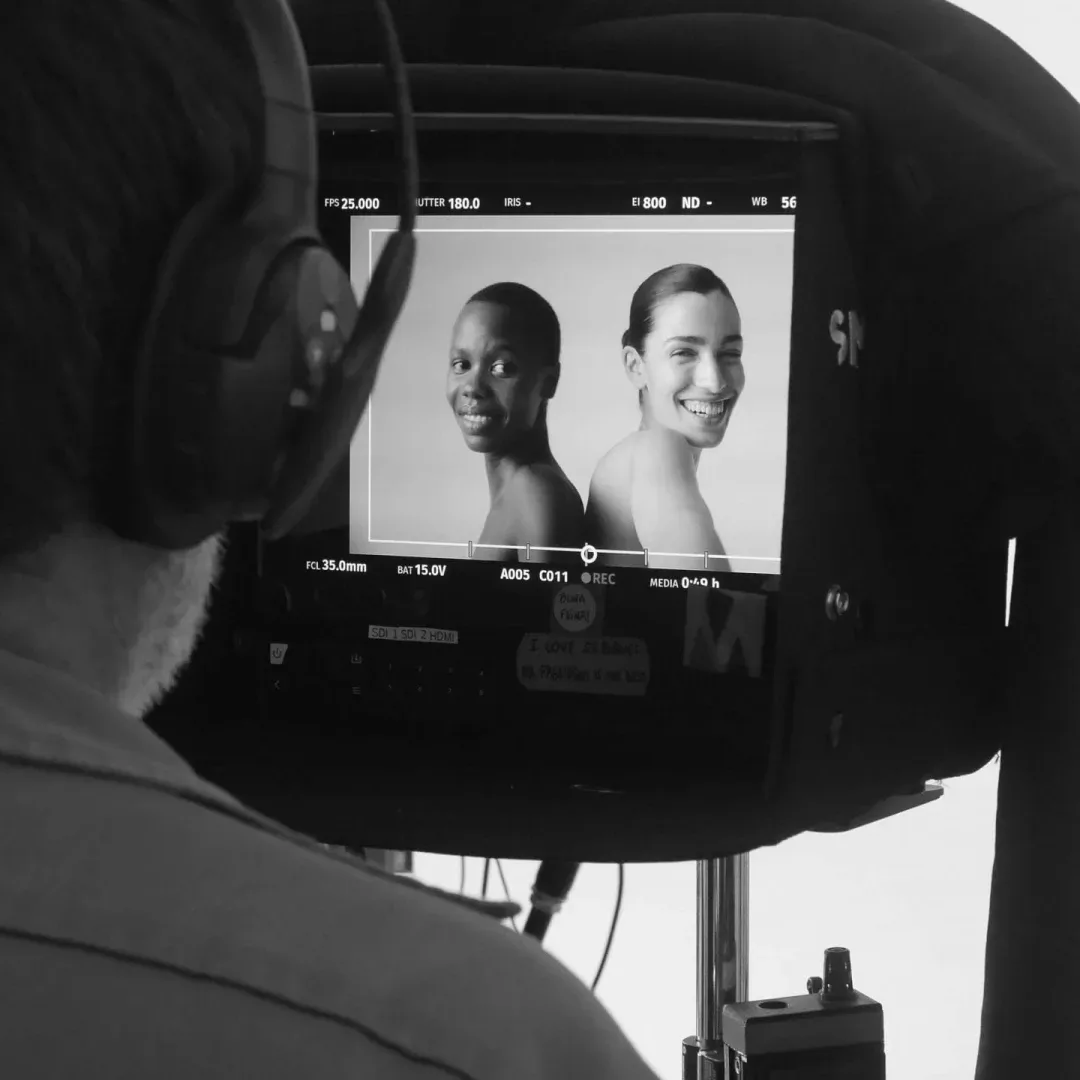 ISDIN Ureadin, making of: un miembro del equipo con auriculares mira a dos modelos en el monitor, en blanco y negro